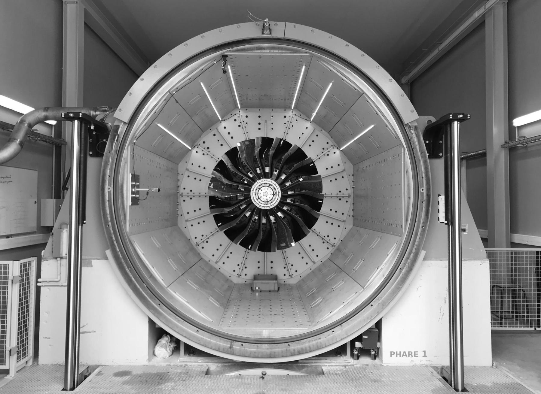 Vue de face de l'enceinte à vide du banc d'essais Phare-1 contenant une soufflante aéronautique (ou fan) composée de 18 pales en matérieu composite. Celle-ci est instruméntée et  excité à l'aide d'un système piézoélectique conçu et mis en peuvre au laboratoire. 